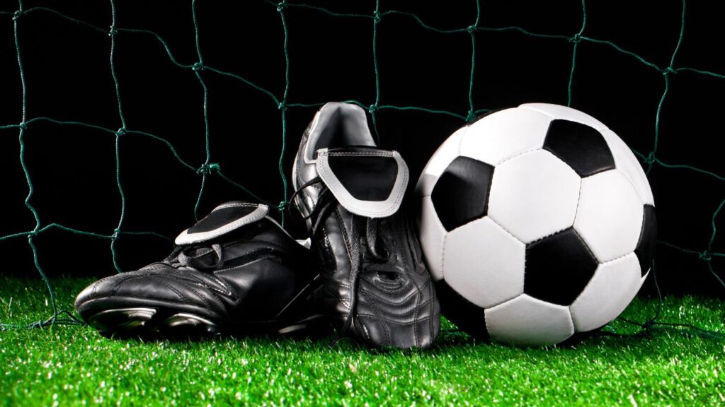 chuteiras ao lado de uma bola de futebol