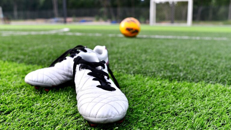 chuteira em campo com bola de futebol ao fundo próximo ao gol