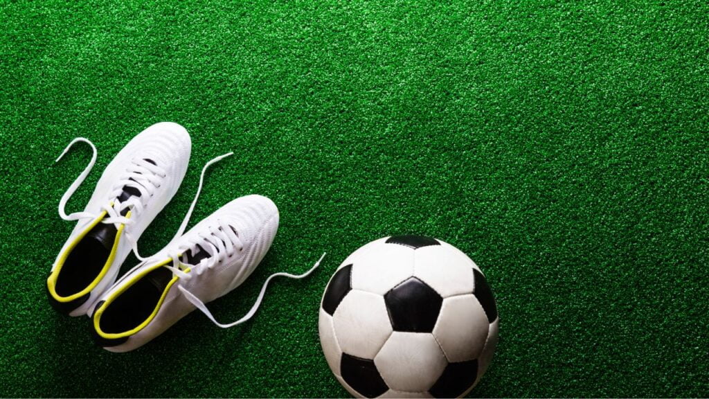 chuteiras em um campo ao lado de uma bola de futebol