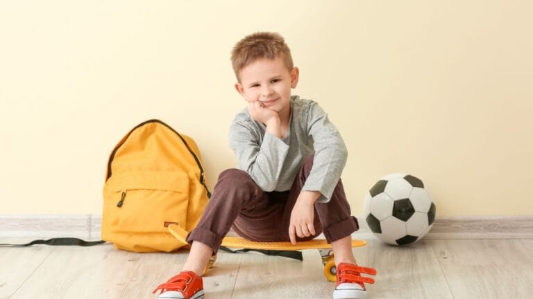 criança sentado ao lado de uma bola de futebol e uma mochila