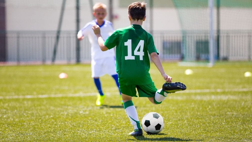 criança chutando bola de futebol